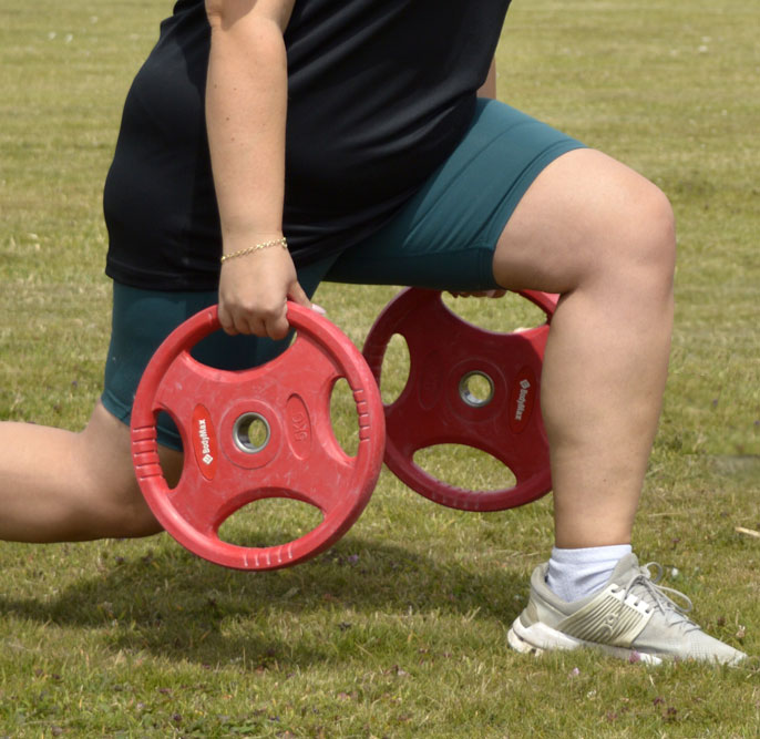 two women in field lunging while holding weights